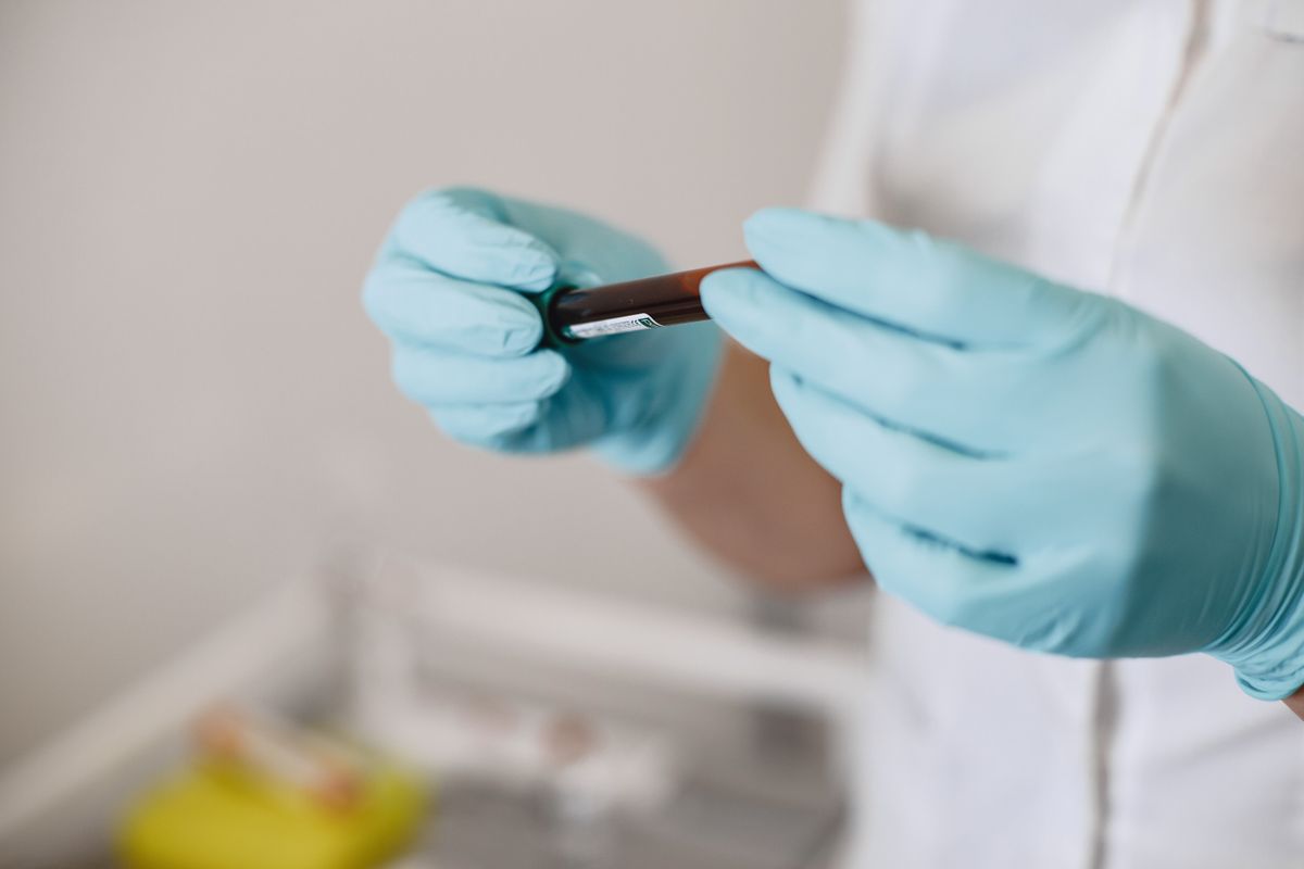 Profissional de saúde de luvas segurando um tubo de coleta de sangue com etiqueta